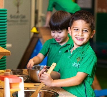 Two children in green British Oak uniforms working with Montessori practical-life materials at a wooden table