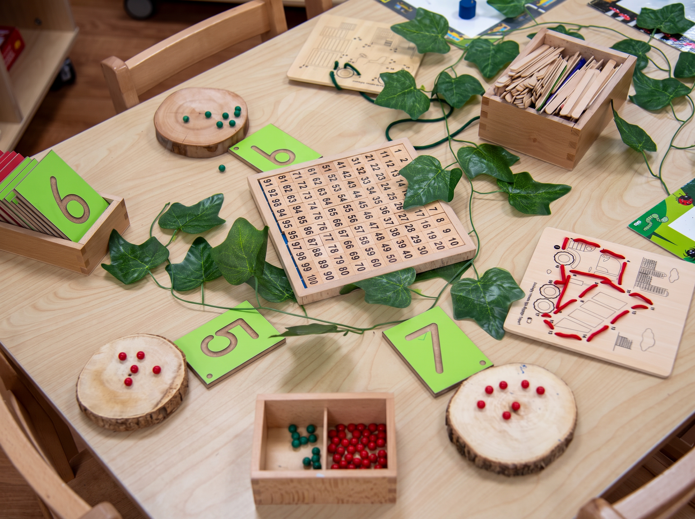 Montessori maths materials — hundred board, number cards and bead counters — laid out on a classroom table